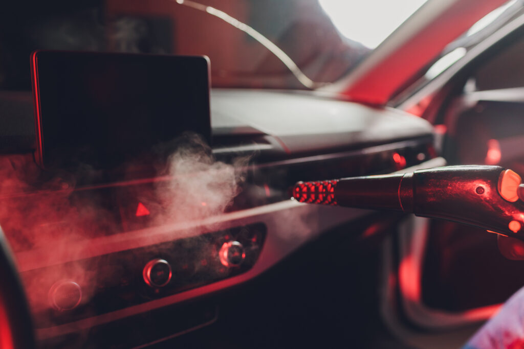 Handsome man cleaning car with hot steam