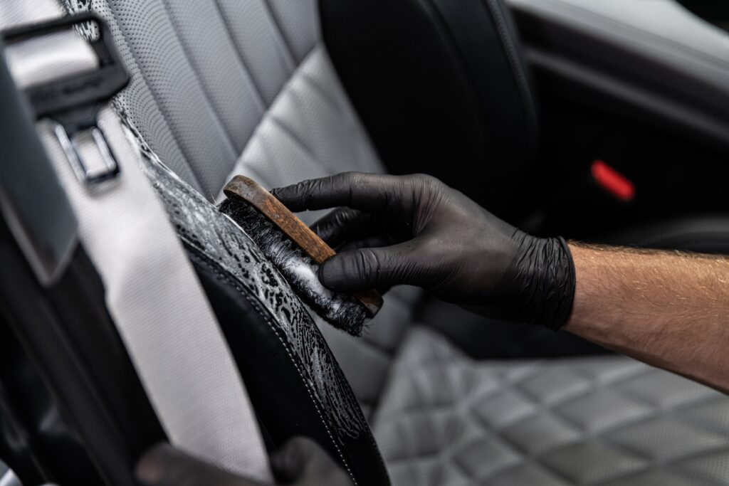 Car detailing studio worker cleaning car interior and car leather seats with a brush. Car wash