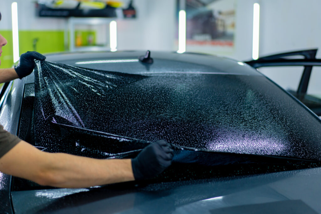 close-up of a car mechanic carefully sticking a protective tinted film on car glass detailing